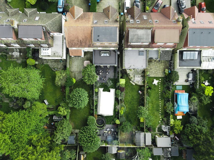 An aerial view of a residential neighborhood showing several small front gardens and backyards. The image features a variety of lush green lawns, neatly trimmed hedges, and mature trees. Some gardens